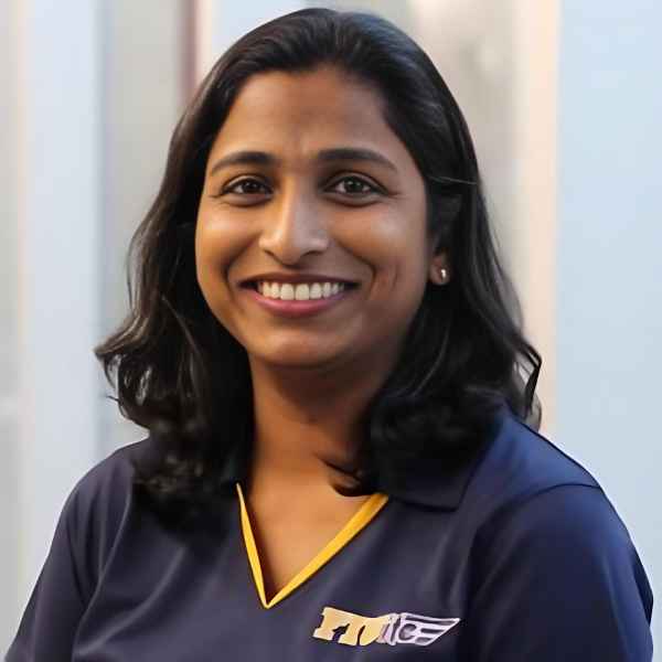 A smiling Indian woman with shoulder-length hair, and a V-neck university-branded shirt