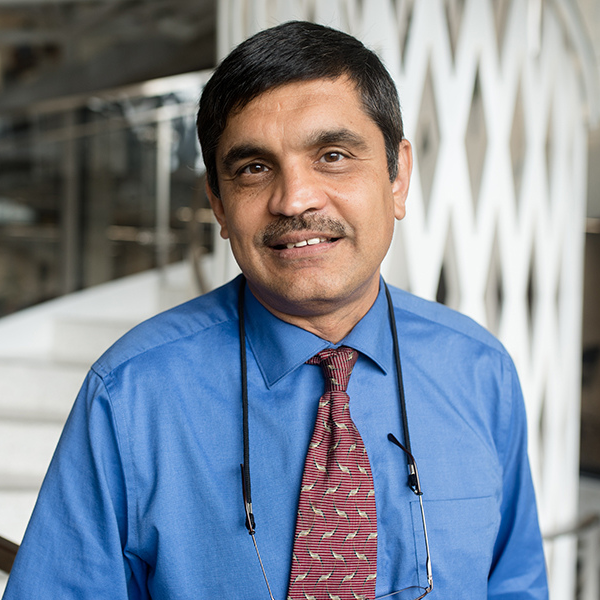 A smiling Indian man with a blue shirt and red tie.