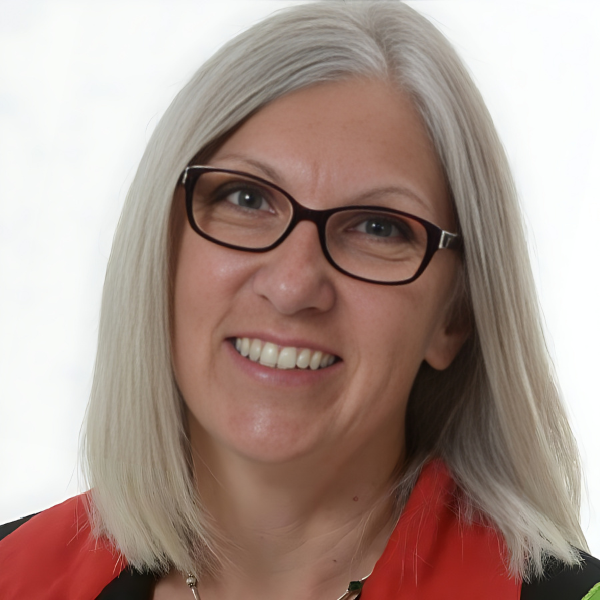 A smiling older white woman with white-blonde hair, brown glasses, and a red shirt