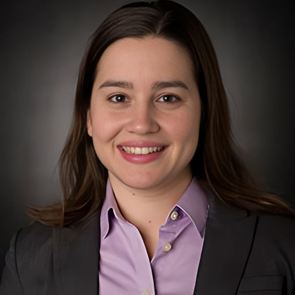 A smiling young Turkish woman with shoulder-length dark hair, a black jacket, and a lavender shirt
