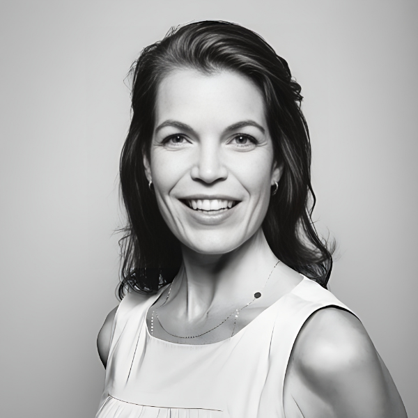 A black and white photo of a smiling middle-aged woman, facing front turned slightly to her right, with shoulder-length brown hair and a white sleeveless shirt