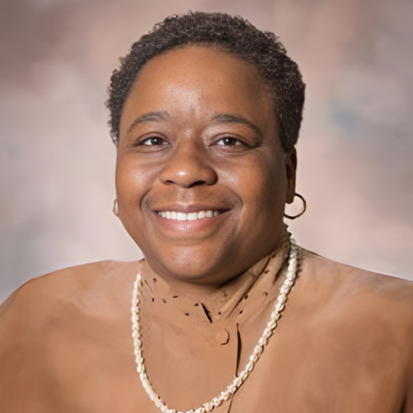 An older African American woman with short hair, a brown shirt, pearls, and small gold hoop earrings
