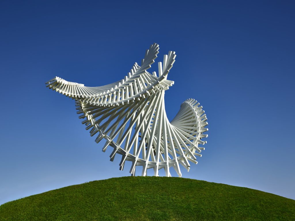 the sweeping side of a sculpture formed from connected long white bars against a blue sky