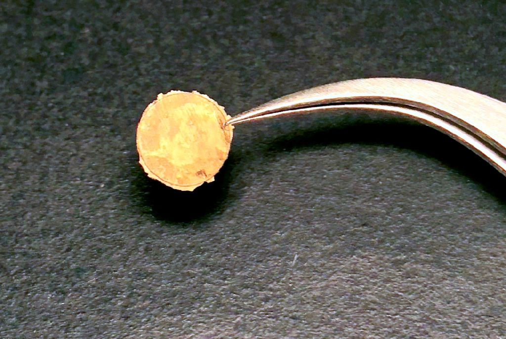 a small gold coin is held by a silver tool